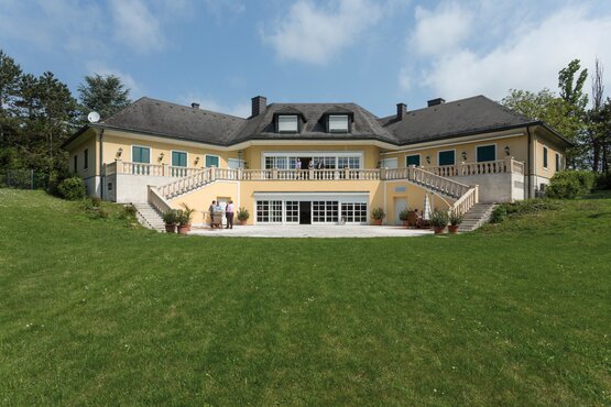 großes gelbes Gebäude mit grüner Wiese in frontaler Ansicht